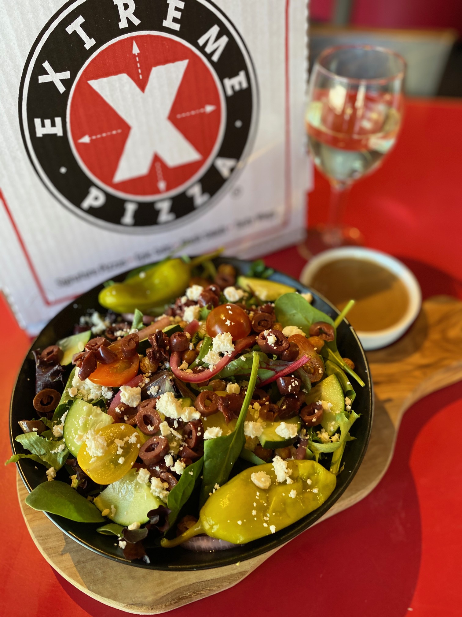 Fresh Extreme Pizza salad with olives, tomatoes, cucumber and feta — alongside the EP menu and a glass of wine